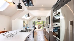 A modern kitchen with a large island, built-in appliances, and a view to the outdoors. - Stylish Family Home With Garden in Peckham Rye (London)
