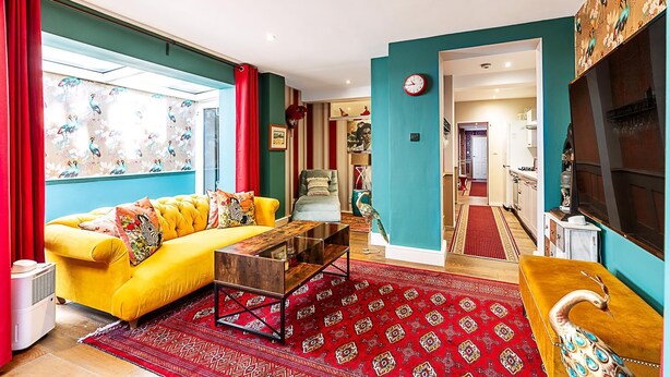 Ein Wohnzimmer mit einem gelben Sofa, einem roten Teppich mit Muster und einer Wand in Türkis.