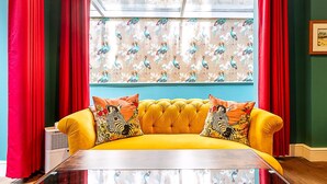 Ein gelbes Sofa mit Kissen in ZEBRA-Muster, rote Vorhänge und ein Fenster mit floralem Druck.