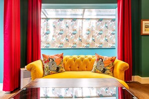 Ein gelbes Sofa mit Kissen in ZEBRA-Muster, rote Vorhänge und ein Fenster mit floralem Druck.