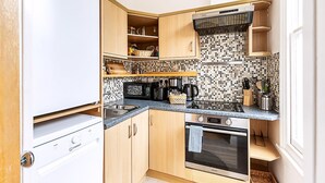 A compact kitchen with wooden cabinets, a microwave, a kettle, and a tiled backsplash. - Contemporary Archway Retreat Near Tube (London)