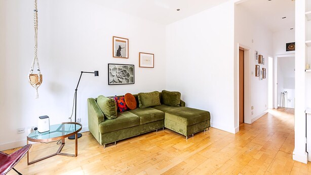 A living room with a green sectional sofa, a glass coffee table, a floor lamp, and framed artwork on the wall. - Contemporary Archway Retreat Near Tube (London)