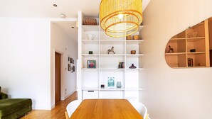 A dining area with a wooden table, white chairs, a green sofa, and a white shelving unit with various items. - Contemporary Archway Retreat Near Tube (London)