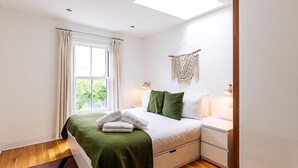 A bedroom with a bed, bedside tables, a window with curtains, a skylight, and a macrame wall hanging. - Contemporary Archway Retreat Near Tube (London)