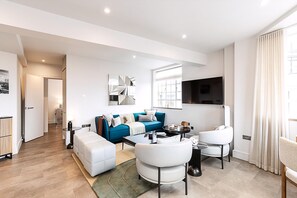 A modern living room with a sofa, chairs, a coffee table, and a TV. - Stylish Chelsea Flat Near Sloane Square (London)
