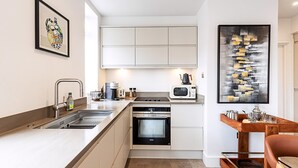 Cocina moderna con horno integrado, microondas y lavaplatos. Se observa una mesa de madera con una bandeja y una silla.