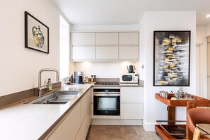 A modern kitchen with a built-in oven, microwave, and sink. There is a wooden table with a tray and a chair. - Stylish Chelsea Flat Near Sloane Square (London)