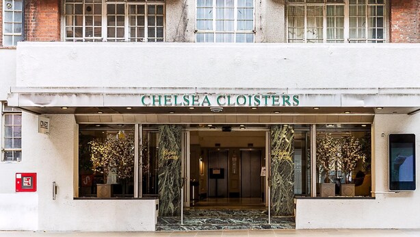 Entrada de un hotel con un cartel que dice 'CHELSEA CLOISTERS', un vestíbulo de mármol y una caja de alarma contra incendios.