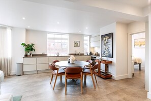 A modern kitchen with a dining area, featuring a round table, chairs, and a large window. - Stylish Chelsea Flat Near Sloane Square (London)