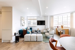 A modern living room with a sofa, coffee table, ottoman, and dining area with chairs and a table. - Stylish Chelsea Flat Near Sloane Square (London)