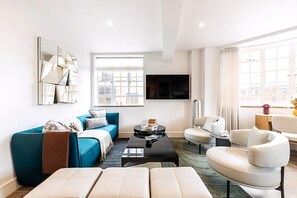 A modern living room with a sofa, coffee table, and chairs, a flat-screen TV, and a large window with a city view. - Stylish Chelsea Flat Near Sloane Square (London)