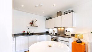 A modern kitchen with white cabinets, a round dining table, and a small orange side table. - Chic East London Stay With Outdoor Space (London)