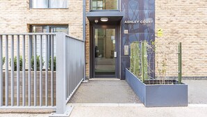 A building entrance with a metal gate, a nameplate reading 'ASHLEY COURT,' and a CCTV sign. - Chic East London Stay With Outdoor Space (London)