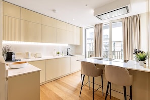 A modern kitchen with white cabinets, a wooden countertop, two bar stools, and a window with curtains. - Contemporary Stratford Escape (London)