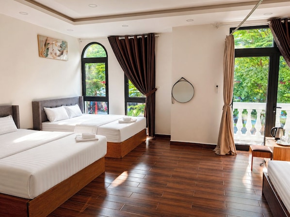 Habitación de hotel con dos camas, un ventanal grande, balcón y un espejo redondo en la pared.