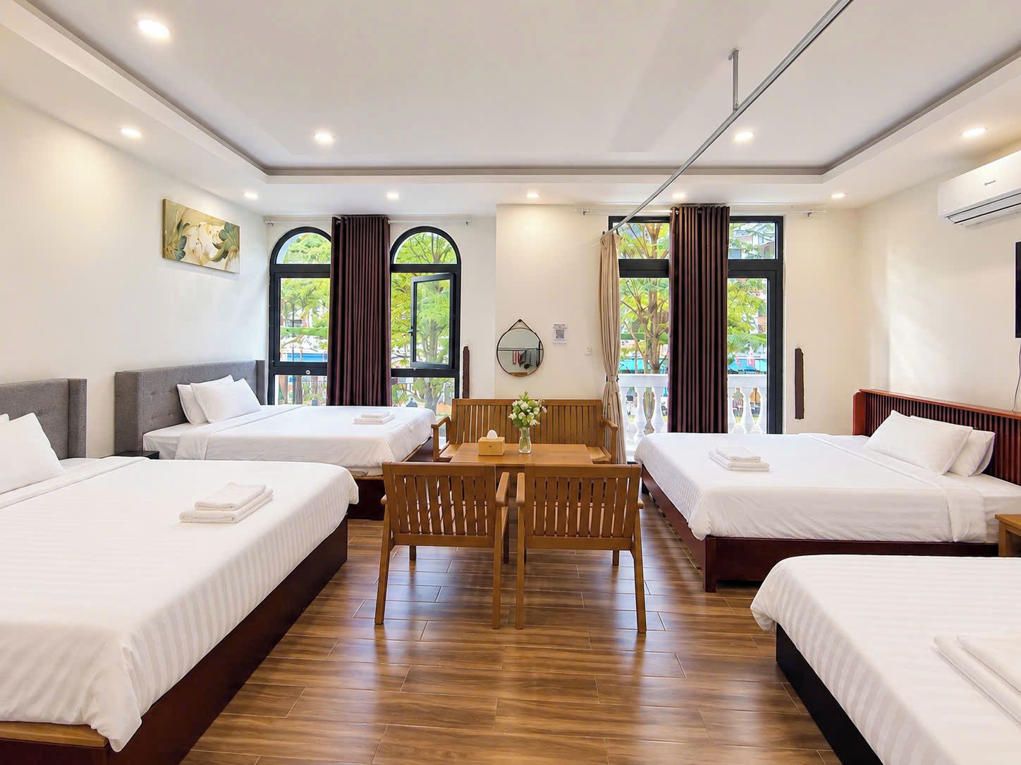 Ein Hotelzimmer mit drei Betten, einem Holztisch und einem Balkon mit Vorhängen.