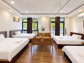Habitación de hotel con tres camas, una mesa de madera y un balcón con cortinas.