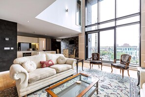 Un salon moderne avec un canapé, des fauteuils, une table basse et de grandes fenêtres donnant sur la ville.