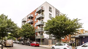 Ein mehrstöckiges Wohngebäude mit Balkonen, parkenden Autos und Bäumen an der Straße.
