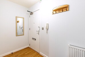 A room with a wooden floor, a white door, a mirror, a light switch, and a radiator. - Modern Mile End Flat With Balcony Terrace (London)