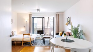 Ein modernes Wohnzimmer mit einer Couch, einem Esstisch, einem Fernseher und einem großen Fenster mit Vorhängen.