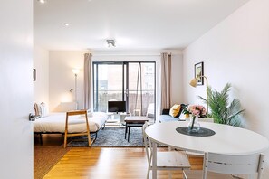 A modern living room with a sofa, a dining table, a TV, and a large window with curtains. - Modern Mile End Flat With Balcony Terrace (London)