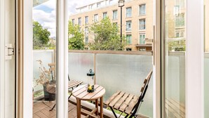 Un balcone con tavolo e sedie, una pianta in vaso e vista su un edificio con numerose finestre.