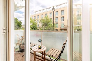 Ein Balkon mit Tisch und Stühlen, einem Blumentopf und Blick auf ein Gebäude mit vielen Fenstern.