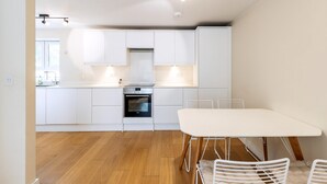 Una cucina moderna con mobili bianchi, forno integrato e zona pranzo con tavolo e sedie bianche.