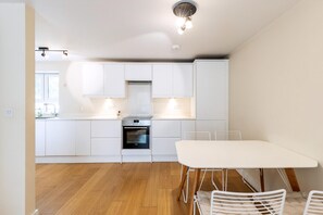 Eine moderne Küche mit weißen Schränken, einem Einbauofen und einem Essbereich mit einem weißen Tisch und Stühlen.