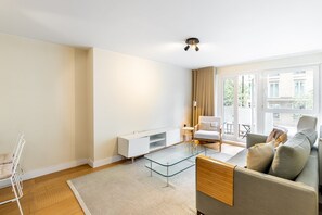 Uma sala de estar moderna com uma mesa de centro de vidro, um sofá, um armário branco e vista para o exterior.
