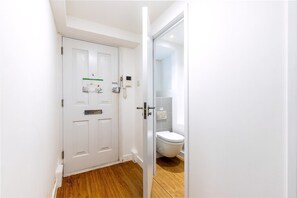 A white door with a phone and a small sign, a wooden floor, and a white toilet. - Belgravia Living 2-bed, 1-bath Apartment With Balcony (London)