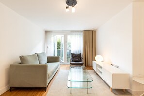 Ein modernes Wohnzimmer mit einer Couch, einem Glastisch, einem Sessel und einem weißen Konsolentisch.