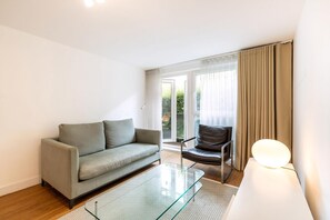 A modern living room with a sofa, a chair, a glass coffee table, and a lamp. - Belgravia Living 2-bed, 1-bath Apartment With Balcony (London)