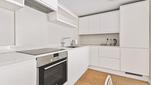 Uma cozinha moderna com armários brancos, forno embutido, pia e chaleira.
