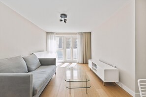 Ein modernes Wohnzimmer mit einer Couch, einem Glastisch, einem weißen Konsolentisch und Blick durch große Fenster.