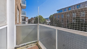Varanda com grade de proteção, vista de edifícios próximos e céu limpo.