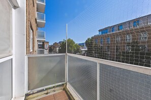 Ein Balkon mit einem Maschendrahtzaun, Blick auf benachbarte Gebäude und einen klaren Himmel.