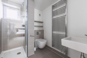 Ein modernes Badezimmer mit Duschkabine aus Glas, Toilette, Waschbecken und Handtuchhalter.