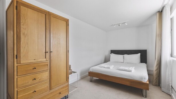 Une chambre avec une grande armoire en bois, un lit avec une literie blanche et une table de chevet.