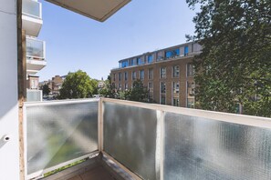 Ein Balkon mit Blick auf ein Backsteingebäude, einen Baum und einen klaren Himmel.