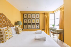 Quarto de hotel com cama, escrivaninha e janela com cortinas.