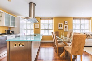 Uma cozinha moderna com uma ilha de vidro, piso de madeira e uma área de refeições com mesa e cadeiras de vidro.