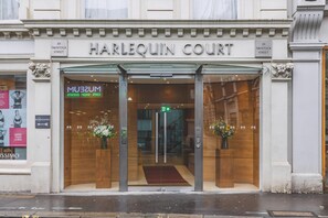 Der Eingang zum Harlequin Court, ein Gebäude mit einer klassischen Fassade, großen Glasfenstern und einem Schild, das auf das Museum und das Café im Inneren hinweist.