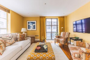 Ein Wohnzimmer mit Sofa, Sessel, Hocker und einem Flachbildfernseher.