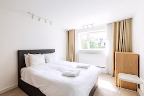 Ein Hotelzimmer mit Bett, einem Fenster mit Vorhängen, einem Holzschrank und einem kleinen Tisch.