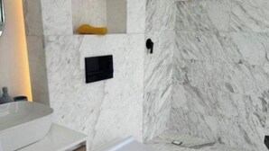 Une salle de bain avec un mur en marbre, des toilettes blanches, un lavabo noir et un meuble en bois.