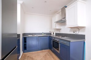 A kitchen with blue cabinets, a stainless steel refrigerator, a built-in oven, and a sink. - Bright 2-bed Apartment in North Acton (London)