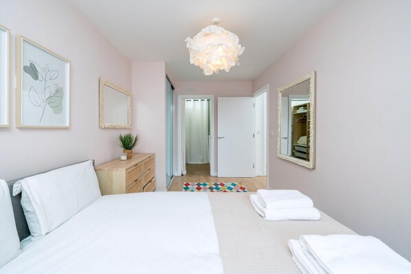 A bedroom with a bed, a dresser, a mirror, a plant, and a hallway leading to a bathroom. - Bright 2-bed Apartment in North Acton (London)