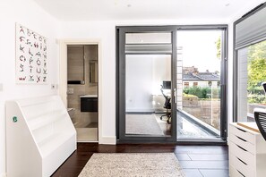 Interior moderno com porta de vidro deslizante para uma varanda, um banco branco e uma obra de arte com o alfabeto fixada na parede.